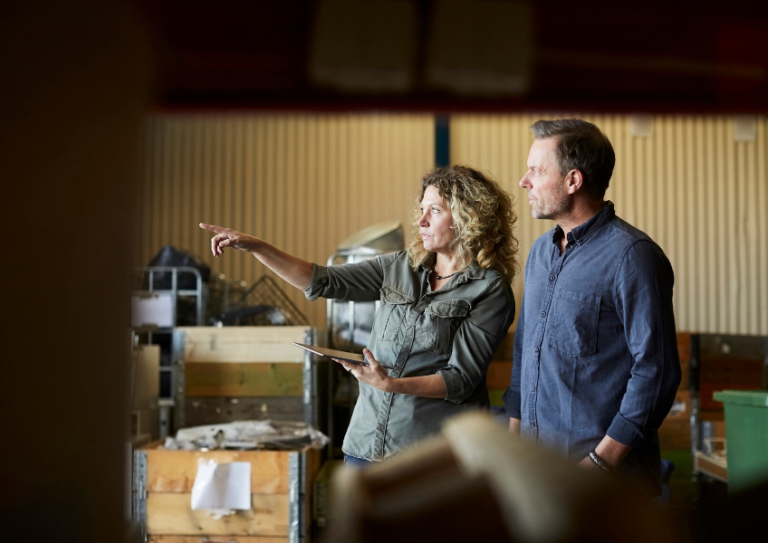 Two business owners work together to reclaim their workspace from clutter. Standing amidst boxes of excess stock, they look at a tablet, discovering a path to better organisation. This photo captures the moment they find Storage King's flexible business storage solutions – a smart, collaborative step towards a more efficient and productive future.